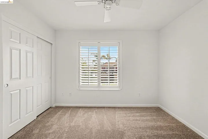 Room featuring neutral carpeting, white walls, and a window with plantation shutters
