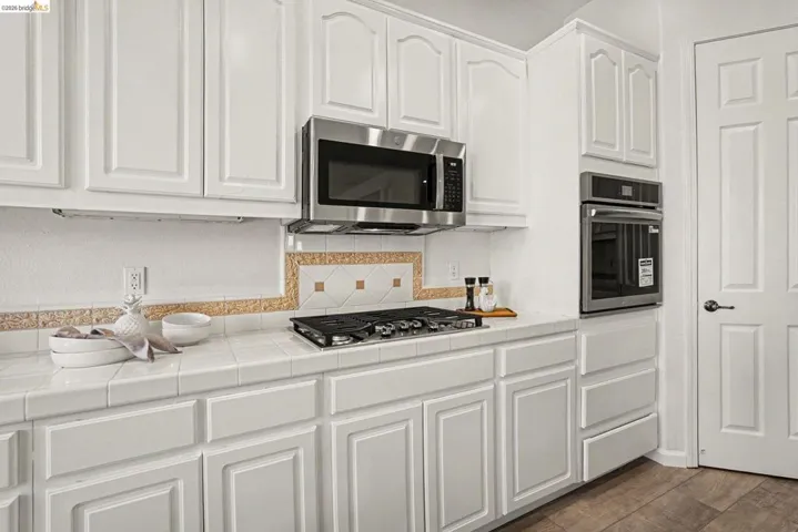 Kitchen featuring white cabinetry, tile countertops, stainless steel microwave, gas cooktop, and built-in oven