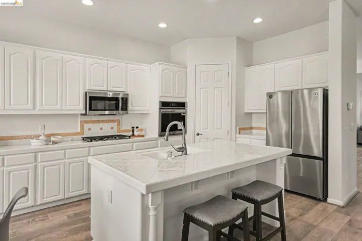 Kitchen featuring white cabinetry, stainless steel appliances, a tiled backsplash, a central island with an integrated sink, and wood-finish flooring
