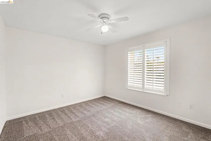 Carpeted interior space featuring a window with white louvered shutters, a ceiling fan with integrated lighting, and neutral wall paint