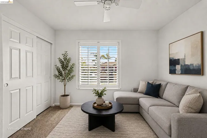 Bright room featuring a ceiling fan, window with plantation shutters, paneled sliding closet doors, and carpet flooring