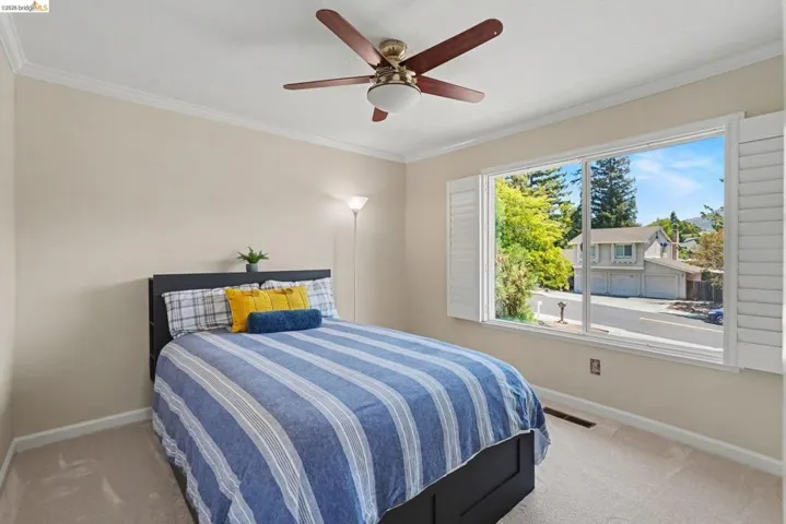 Bedroom featuring a window with white plantation shutters, crown molding, and a ceiling fan with light fixture