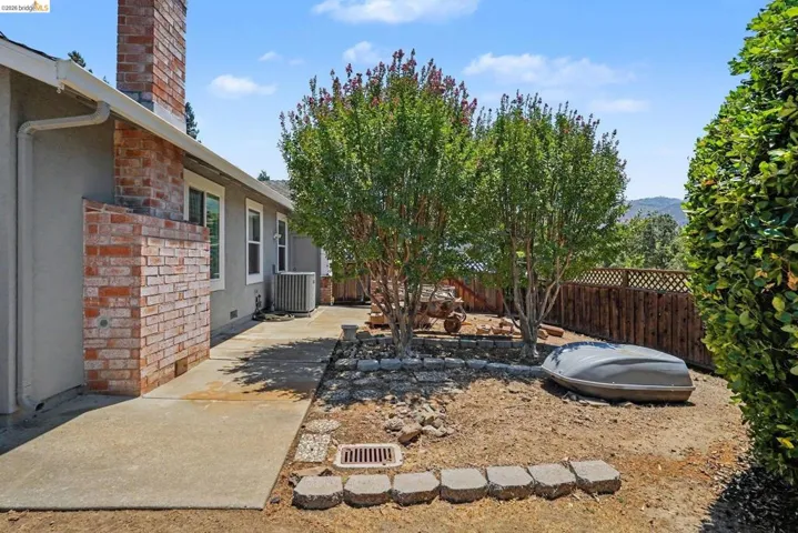 Side yard featuring a concrete walkway, brick chimney, stucco siding, and a wooden fence