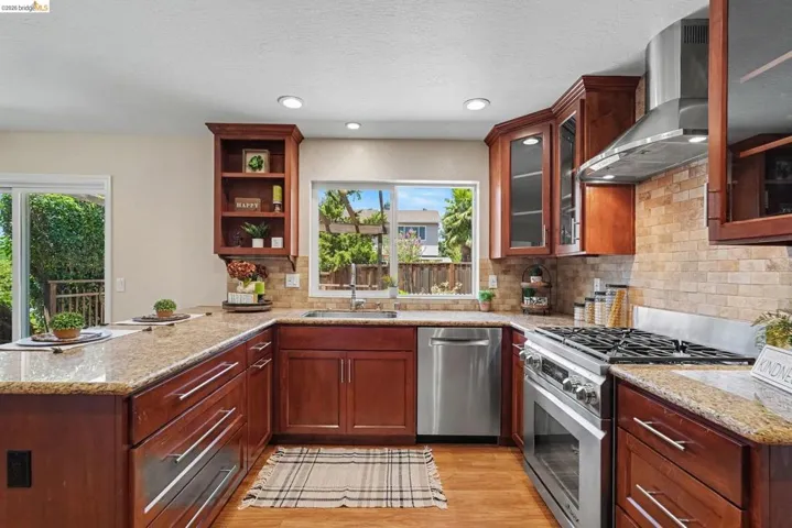 U-shaped kitchen featuring wood cabinetry, granite countertops, tile backsplash, and stainless steel appliances