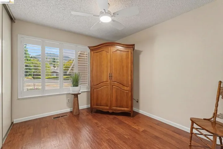 Window with interior plantation shutters, wood-finish flooring, ceiling fan with light, and light-colored walls