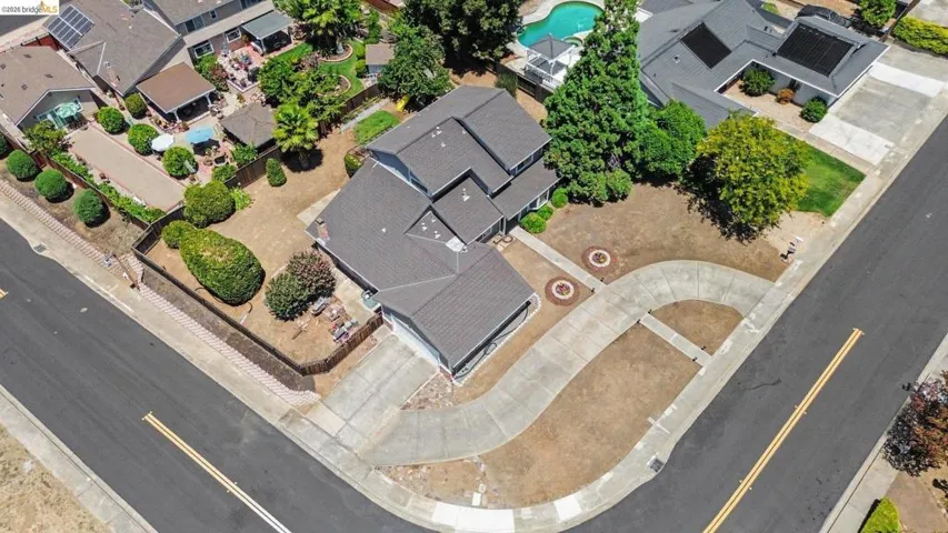 Aerial perspective showcasing a property with a dark shingled roof, an attached garage, and a concrete driveway