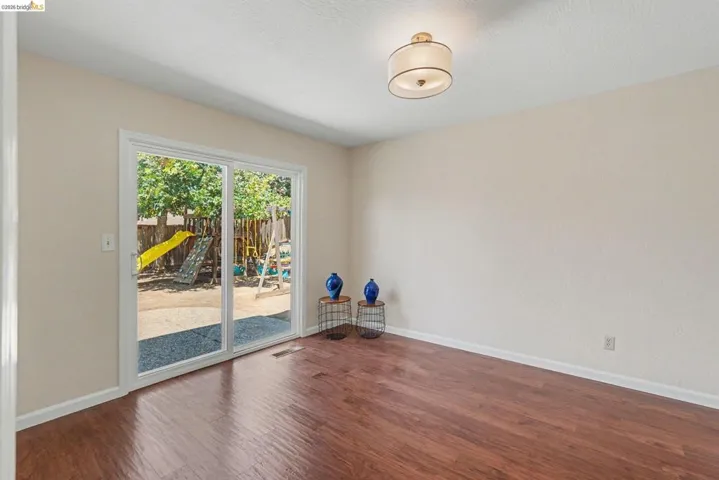 Spacious room featuring wood-finish flooring, light-colored walls, and a contemporary ceiling light fixture