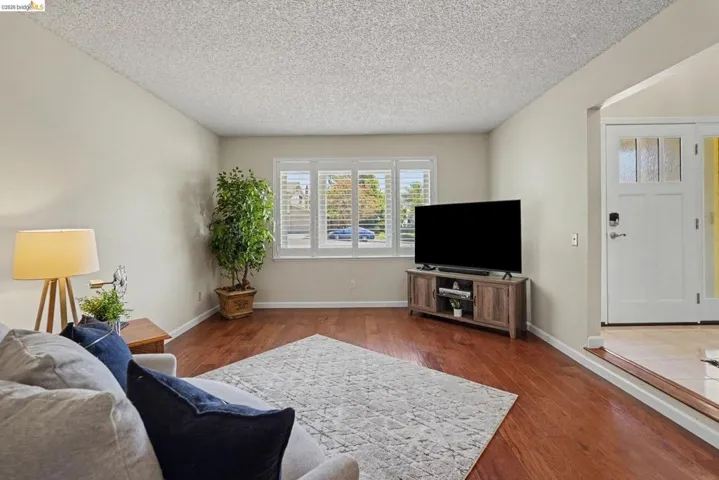 Living area featuring wood-finish flooring, a front entry door with glass paneling, and a wide window with interior plantation shutters