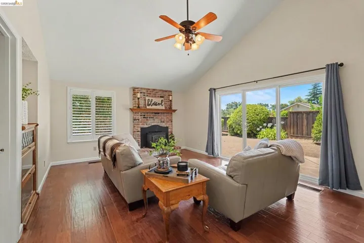 Vaulted ceiling living space featuring wood-finish flooring, a brick fireplace with mantel, and a ceiling fan