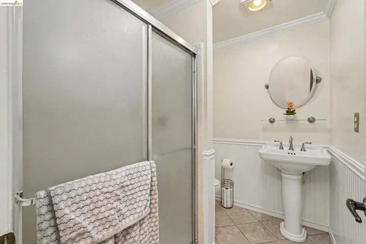 Bathroom featuring a pedestal sink with a chrome faucet, a circular mirror, and a glass shelf