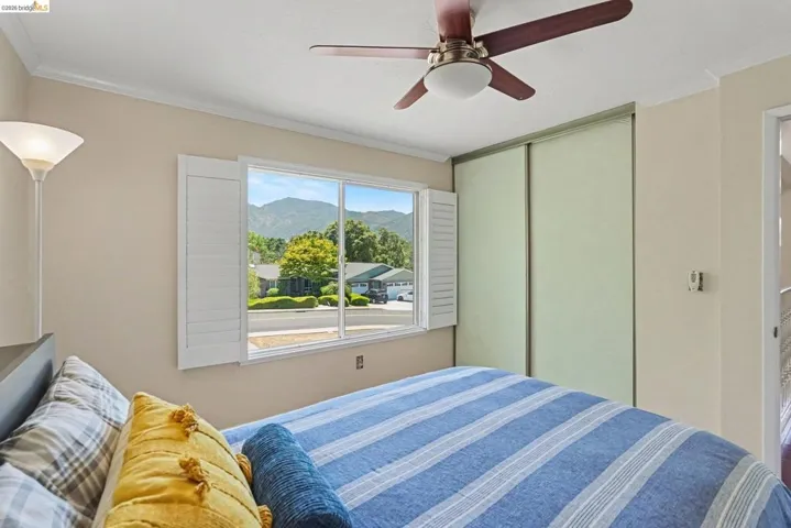 Room featuring a window with white shutters, a ceiling fan with wood-finish blades, and sliding closet doors