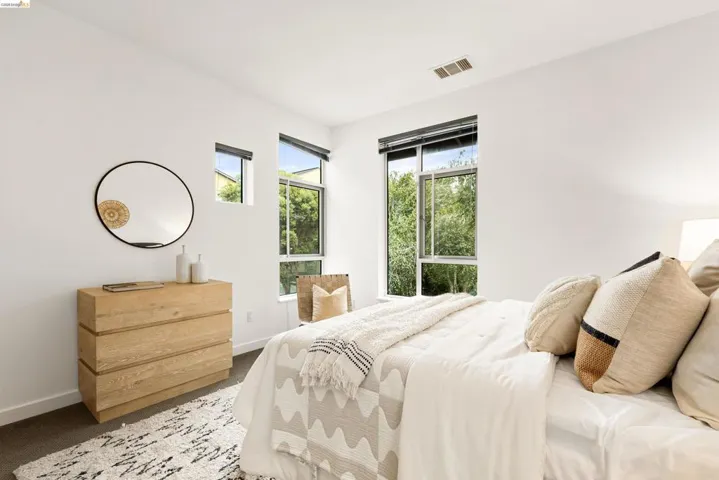 Bright interior space featuring multiple windows with dark roller shades, a contemporary wood-finish dresser, and dark carpeting