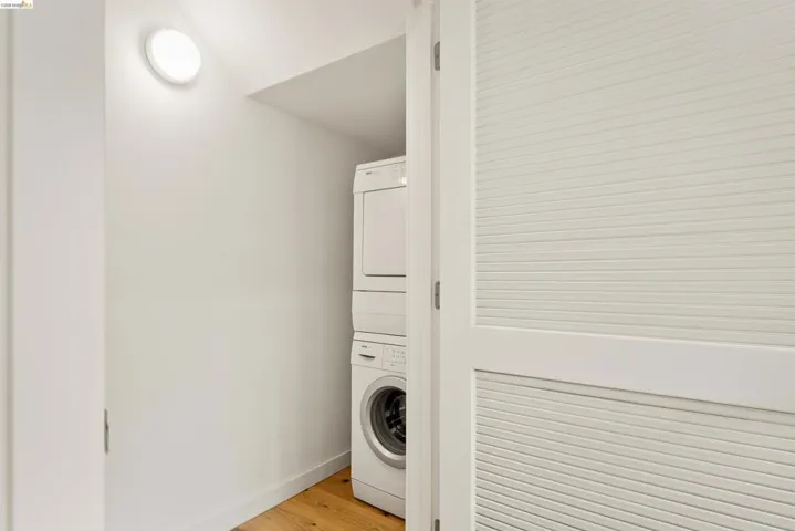 Dedicated laundry area featuring a stacked washer and dryer unit, wood-finish flooring, a wall-mounted light fixture, and louvered bi-fold doors