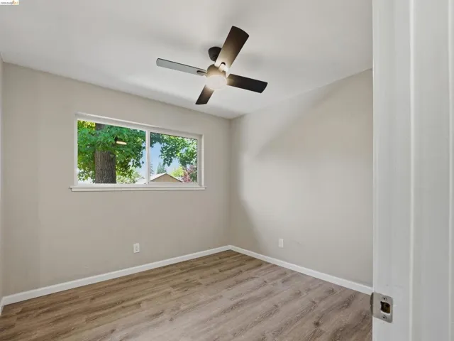 Room featuring wood-finish flooring, a contemporary ceiling fan with integrated lighting, a rectangular window, and neutral wall paint