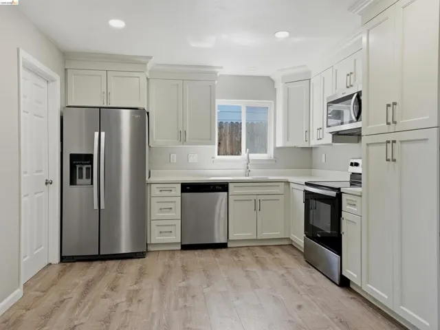 Kitchen featuring white shaker-style cabinetry, light-toned countertops, stainless steel appliances, and wood-finish flooring