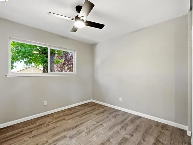 Room featuring wood-finish flooring, light gray walls, white trim, and a ceiling fan with integrated lighting
