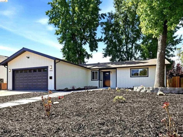 Single-story residence featuring white vertical siding with dark trim accents and a dark paneled garage door