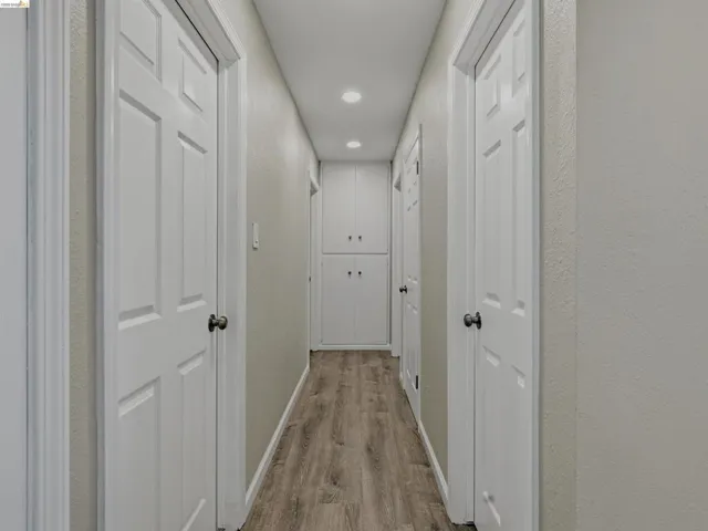 Hallway featuring wood-finish flooring, recessed lighting, and bright white panel doors with black hardware