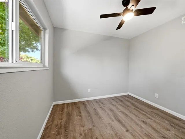 Interior room with wood-finish flooring, light grey walls, and a ceiling fan with integrated lighting