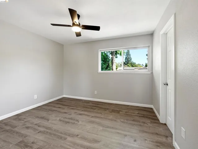 Neutral-toned room featuring wood-finish flooring, a contemporary ceiling fan with integrated lighting, a white trim window, and a paneled interior door
