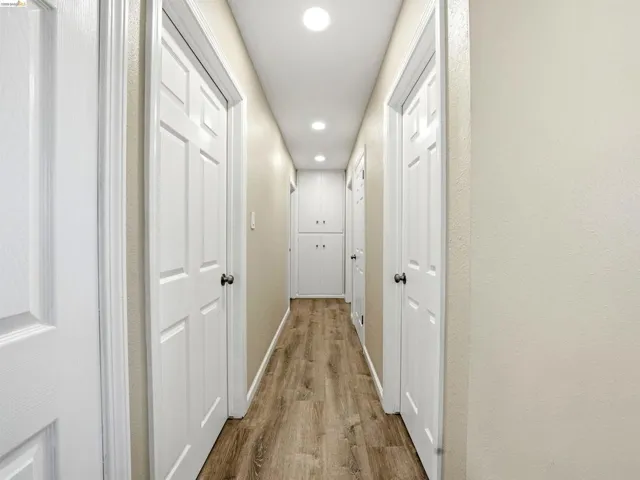 Hallway featuring wood-finish flooring, recessed lighting, and built-in white cabinetry at the far end