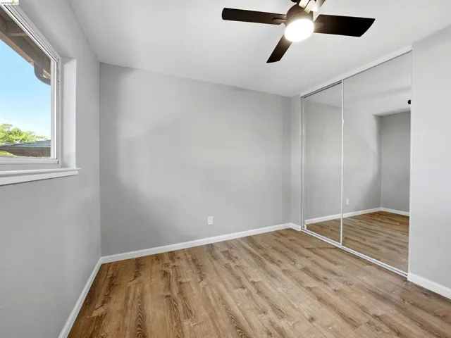 Room with wood-finish flooring, a ceiling fan with integrated lighting, and a mirrored closet