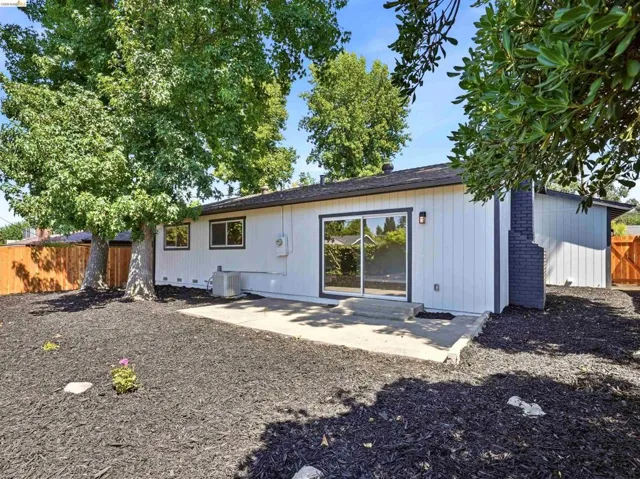 Rear exterior showcasing a sliding glass door, a concrete patio, and a dark brick chimney