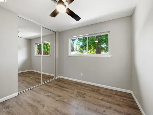 Bedroom featuring wood-finish flooring, two large windows, a ceiling fan with integrated lighting, and mirrored closet doors