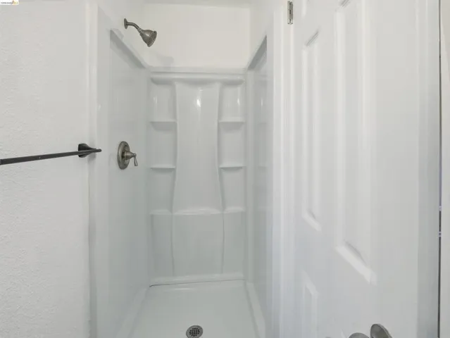 White shower stall featuring an integrated shelving unit and brushed nickel fixtures
