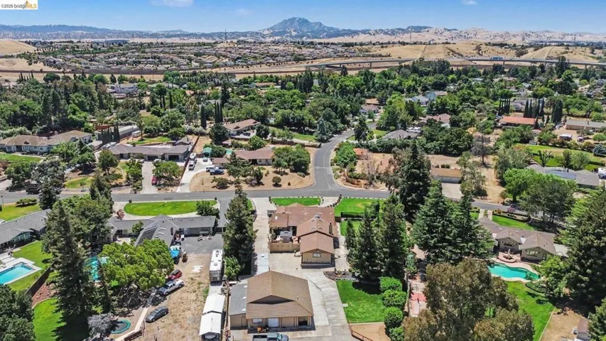 Neighborhood aerial featuring multiple single-family homes, mature trees, and private swimming pools
