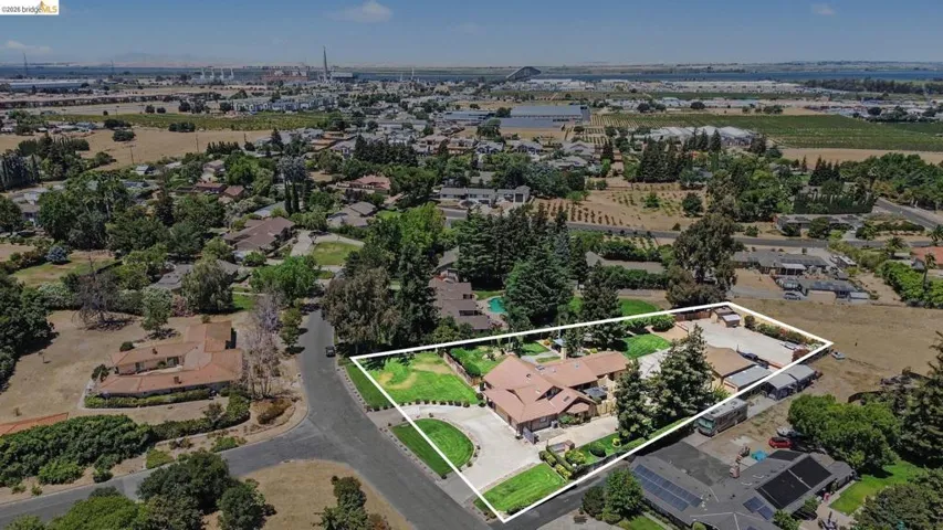 Expansive property featuring a Mediterranean-style residence with a terracotta tile roof, a circular driveway, mature landscaping, and a substantial paved utility area