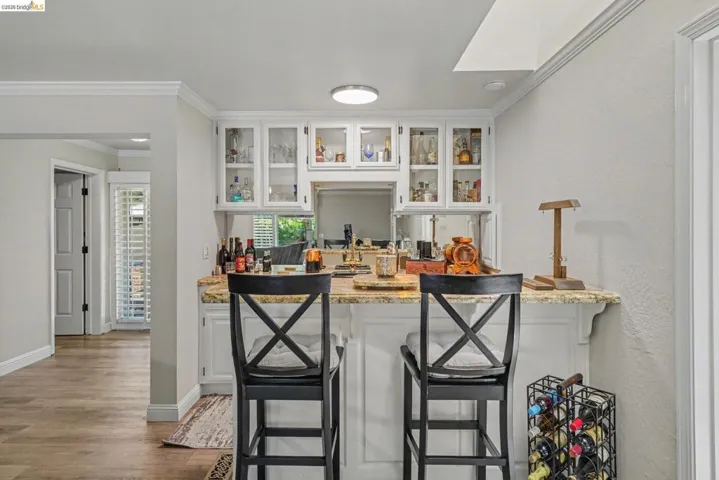 Built-in bar featuring a granite countertop, white cabinetry with glass-front uppers, and wood-finish flooring