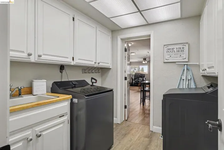 Laundry room featuring white cabinetry, a utility sink with a wood-finish countertop, and wood-finish flooring
