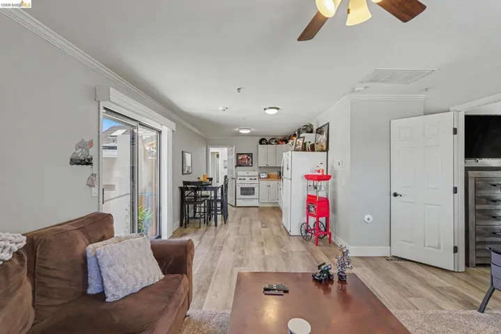 Open-concept living space featuring wood-finish flooring, crown molding, and a ceiling fan with integrated lighting