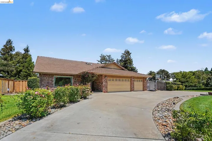 Brick-front residence featuring a tile roof, an attached two-car garage with wood-finish doors, and a concrete driveway