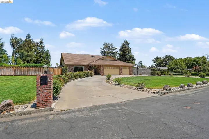 Brick exterior home with an attached two-car garage, featuring a paved driveway, mature landscaping, and a manicured lawn