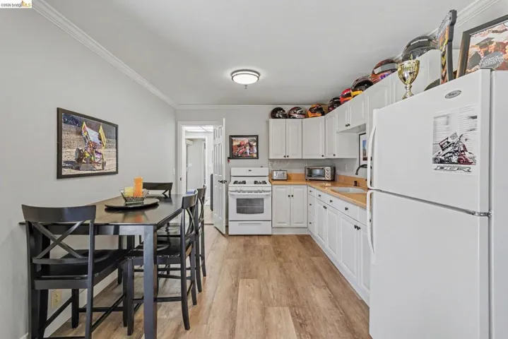 Open-concept kitchen and dining area featuring wood-finish flooring, white cabinetry, light countertops, a white refrigerator, and a white gas range
