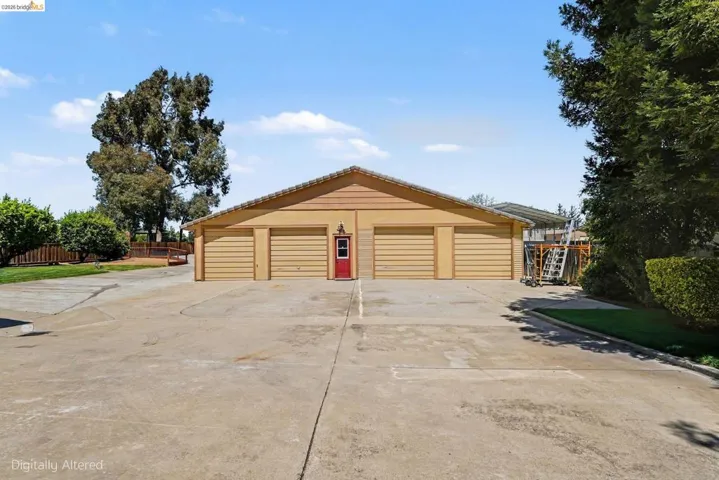 Expansive driveway leading to a three-car garage with horizontal panel doors and a central red entry door