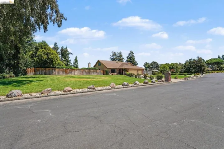 Sprawling ranch-style residence featuring a prominent front lawn, mature trees, and a private wooden fence