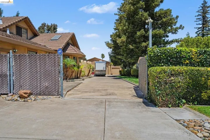 Expansive concrete driveway with a chain-link fence, mature hedges, and established​​‌​​​​‌​​‌‌​​‌​​​‌‌​​​‌​​‌‌​​‌‌​​‌‌​​​​ trees