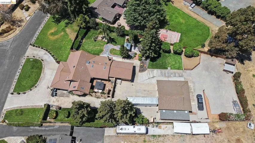 Expansive property featuring a large residence with a multi-gabled roof, extensive paved driveways, a detached outbuilding, a basketball court, and mature landscaping