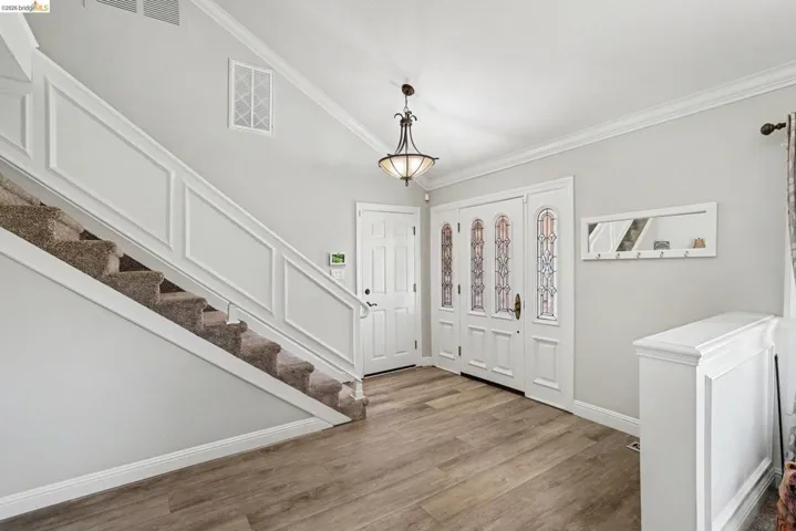 Entry foyer featuring wood-finish flooring, a multi-panel front door with decorative glass inserts, a carpeted staircase with wainscoting, a flush-mount chandelier, and crown molding