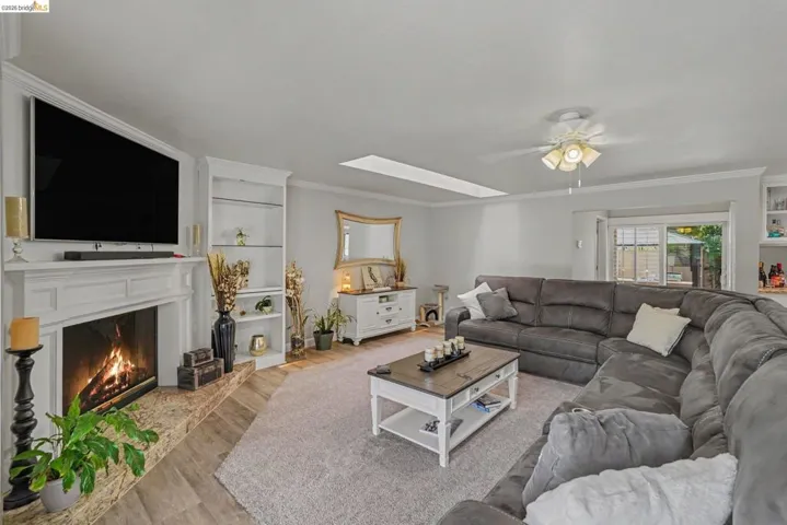Living area featuring a white fireplace mantel with a stone hearth, built-in shelving, wood-finish flooring, a ceiling fan, and a skylight