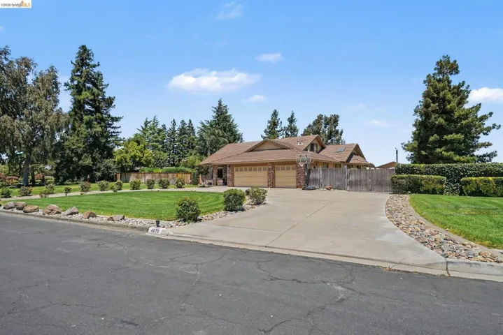 Suburban residence featuring a multi-car driveway, a meticulously landscaped front lawn, mature trees, and a decorative rock border