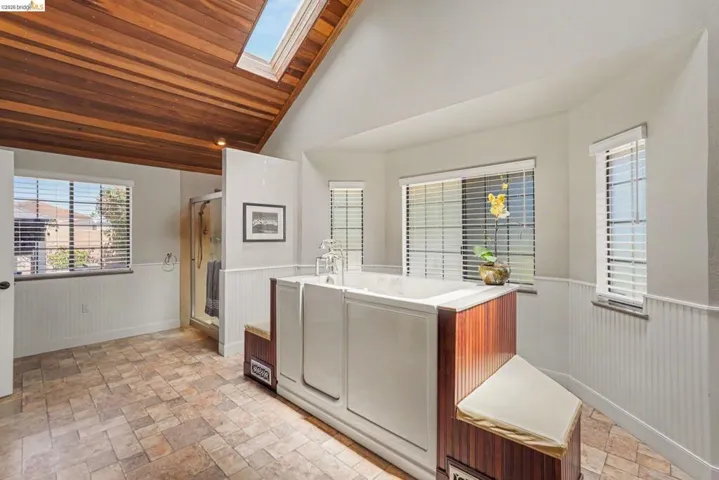 Spacious bathroom featuring a walk-in tub with a wood-finish surround, a skylight, a glass-enclosed shower, and a wood plank ceiling