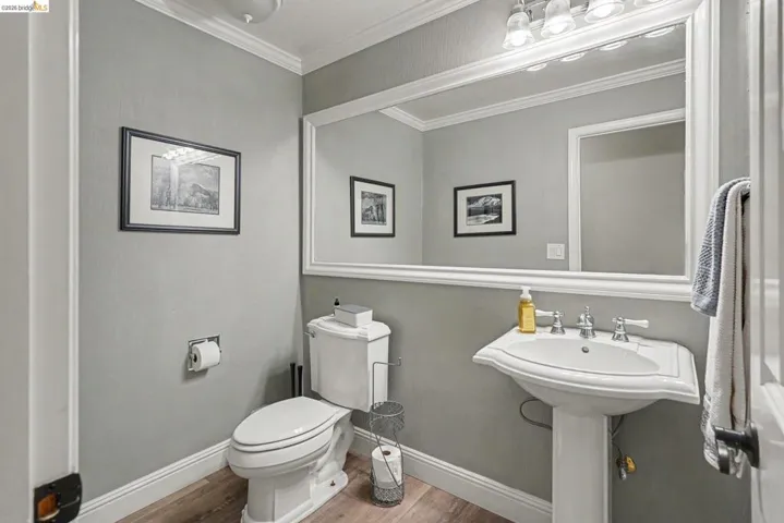 Pedestal sink with dual-handle faucet, large framed mirror, vanity lighting, and wood-finish flooring