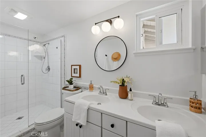 Functional primary bathroom with dual sinks, window for ventilation, and walk-in shower