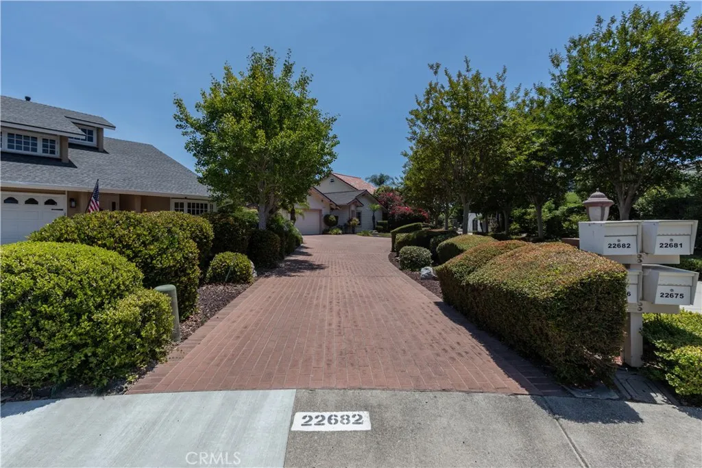 Flag lot with paver driveway lined by well manicured shrubs.