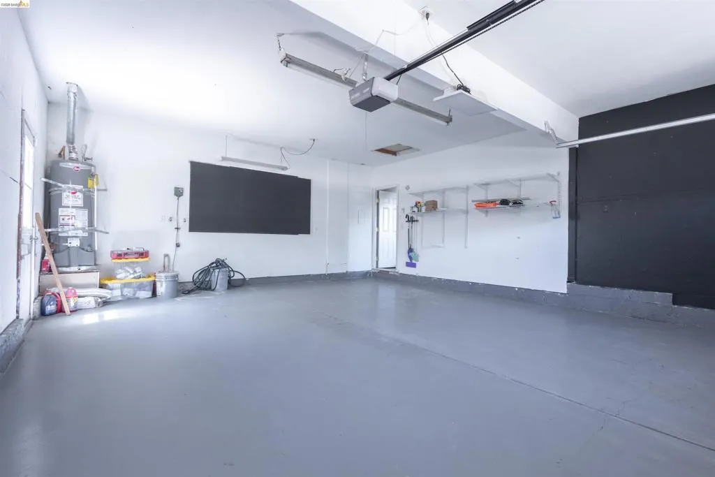 Spacious garage with light gray finished flooring, white painted walls, exposed ceiling joists, and track lighting