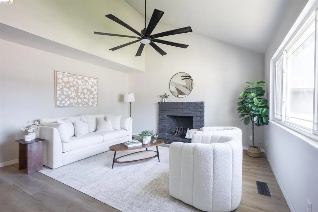 Vaulted ceiling with a large ceiling fan, gray brick fireplace, and wood-finish flooring
